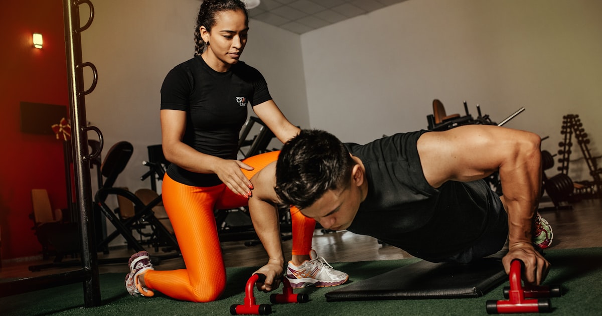 Personal trainer che segue un cliente durante un esercizio in palestra, a rappresentare il codice ateco personal trainer forfettario
