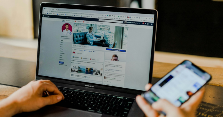Social media manager al lavoro su laptop e smartphone, gestendo una pagina social per un cliente in regime forfettario